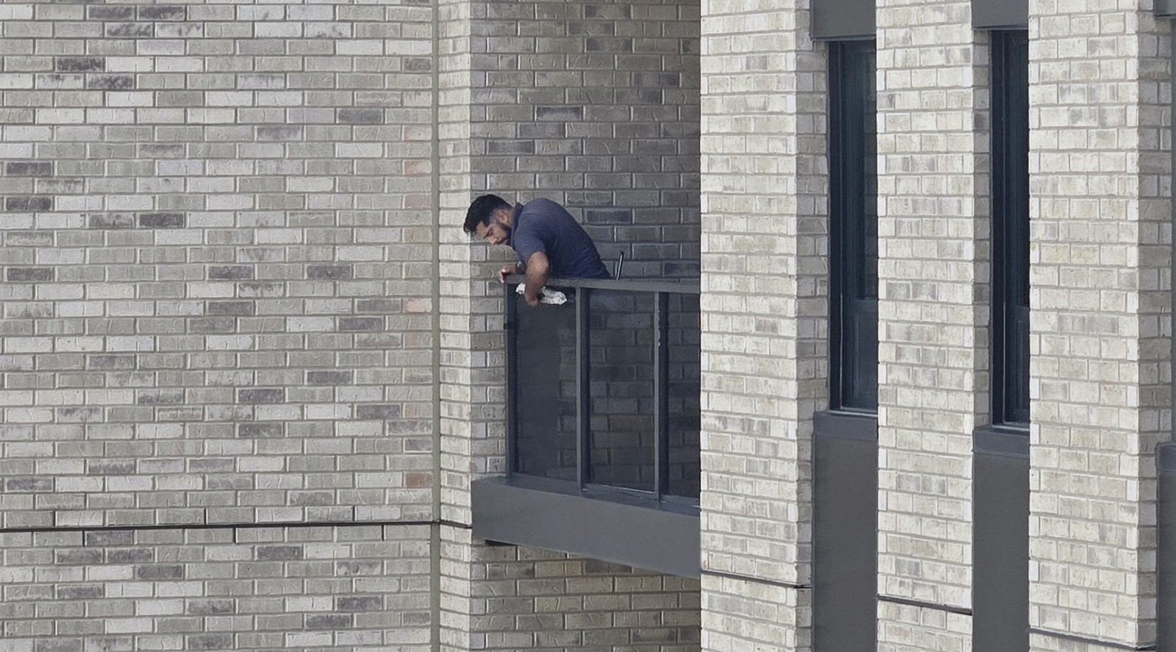 Window cleaner detailing balcony glass at a multi-storey retirement residence